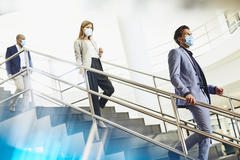 Three people walking down the stairs at a office, wearing face masks.