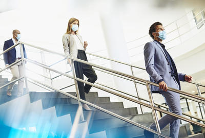 Three people walking down the stairs at a office, wearing face masks.